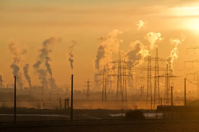 Factories in the distance send plumes of smoke into a foggy orange sky.