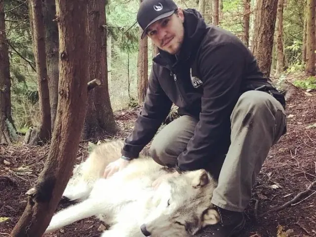 Visitor seated with a wolf in a forest clearing