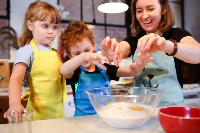 An adult helps children stir ingredients in a mixing bowl