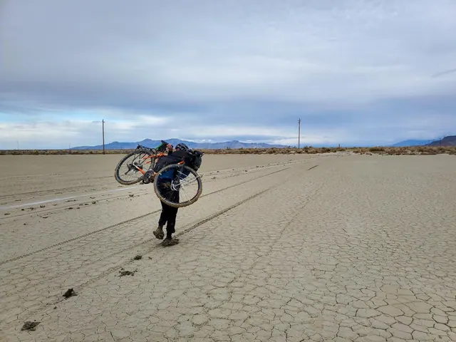 Person carrying a bicycle across a dry lakebed