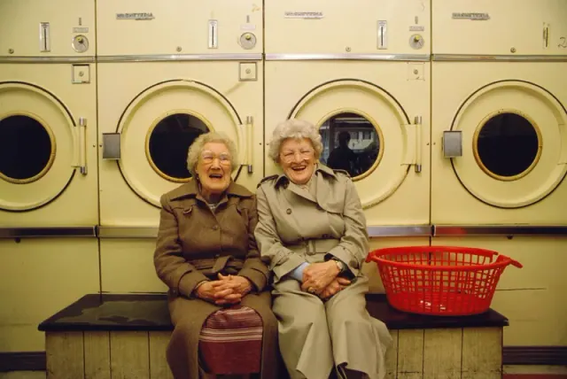 Two women seated in front of laundry machines