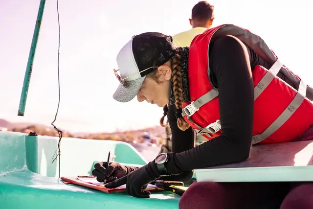 A person wearing a life jacket writing aboard a boat