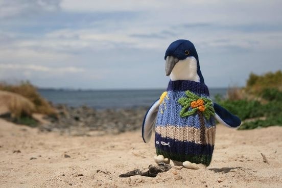 A plush penguin toy in a blue jumper with a knitted flower.