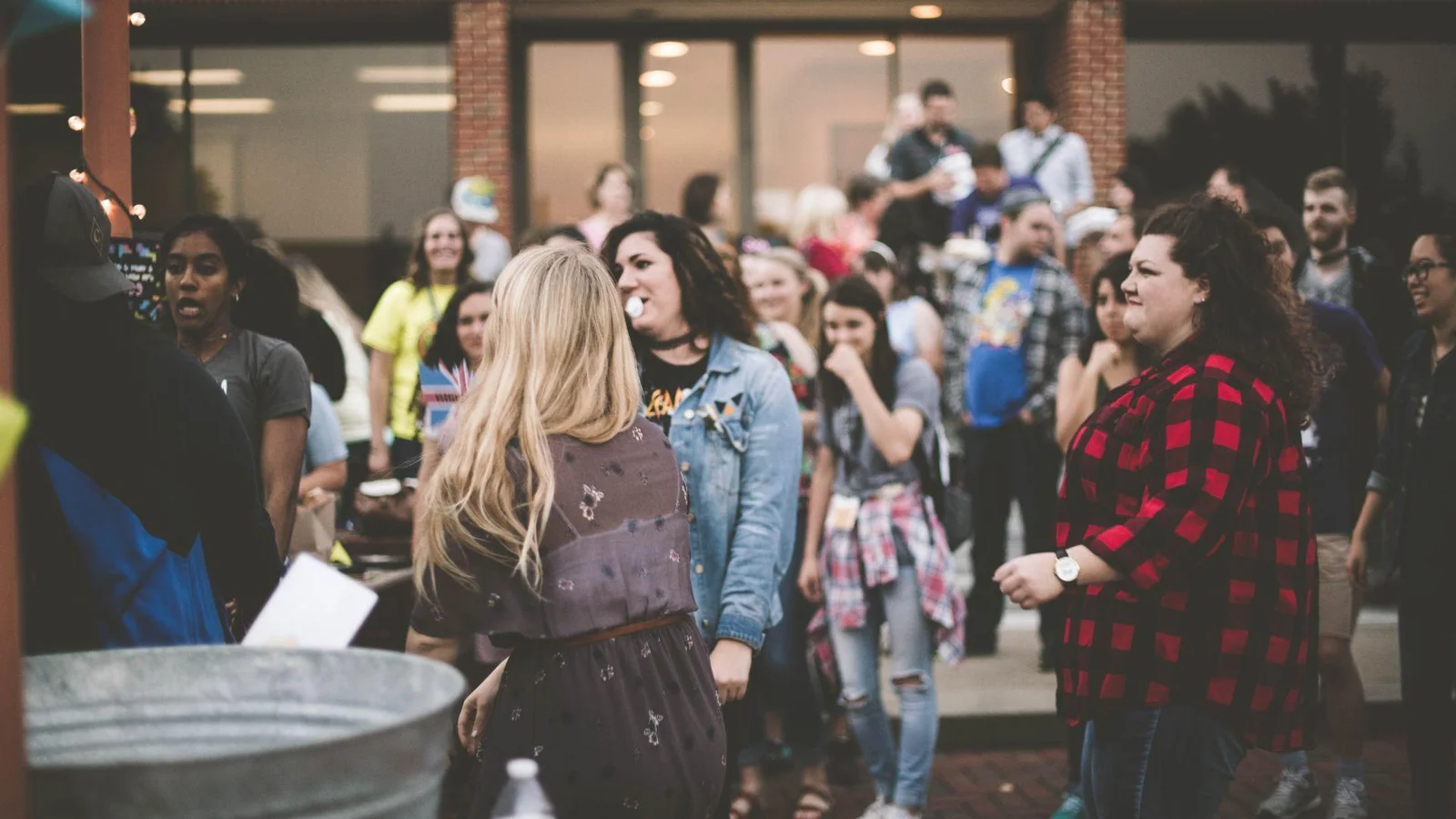 A diverse group of people socializing outside a brick building. Several people are engaged in conversations