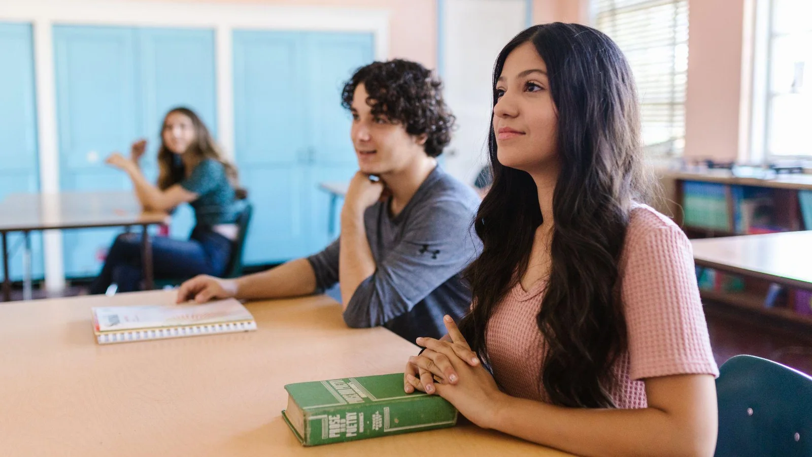Two students sitting at desks in a classroom, focusing on something in front of them