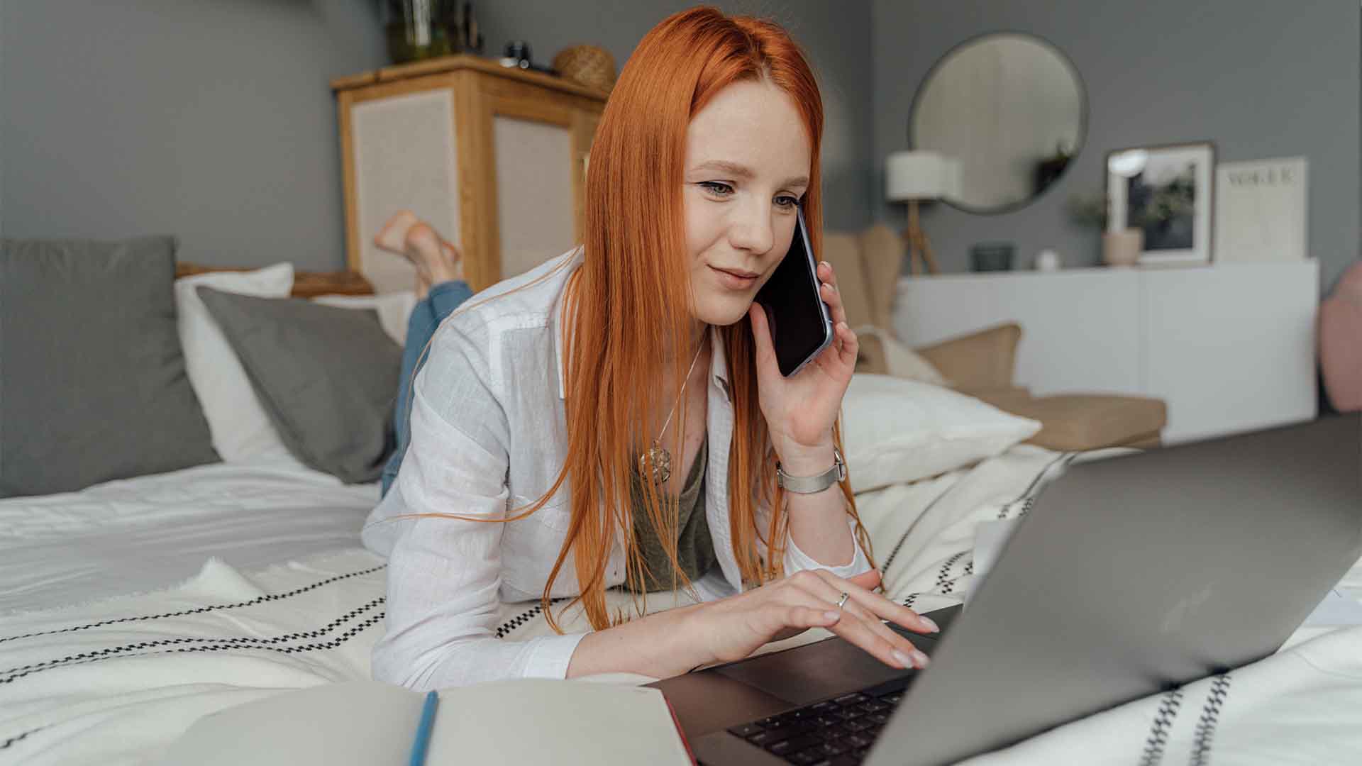 Illustrative photograph of a person using a phone beside a laptop.