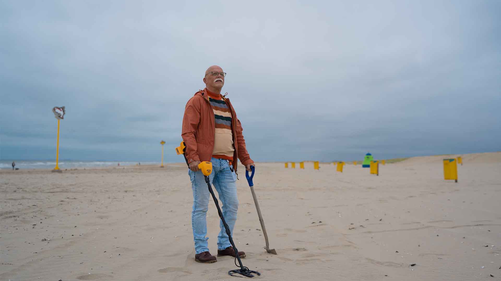 Illustrative photograph of a person using a metal detector on a beach.