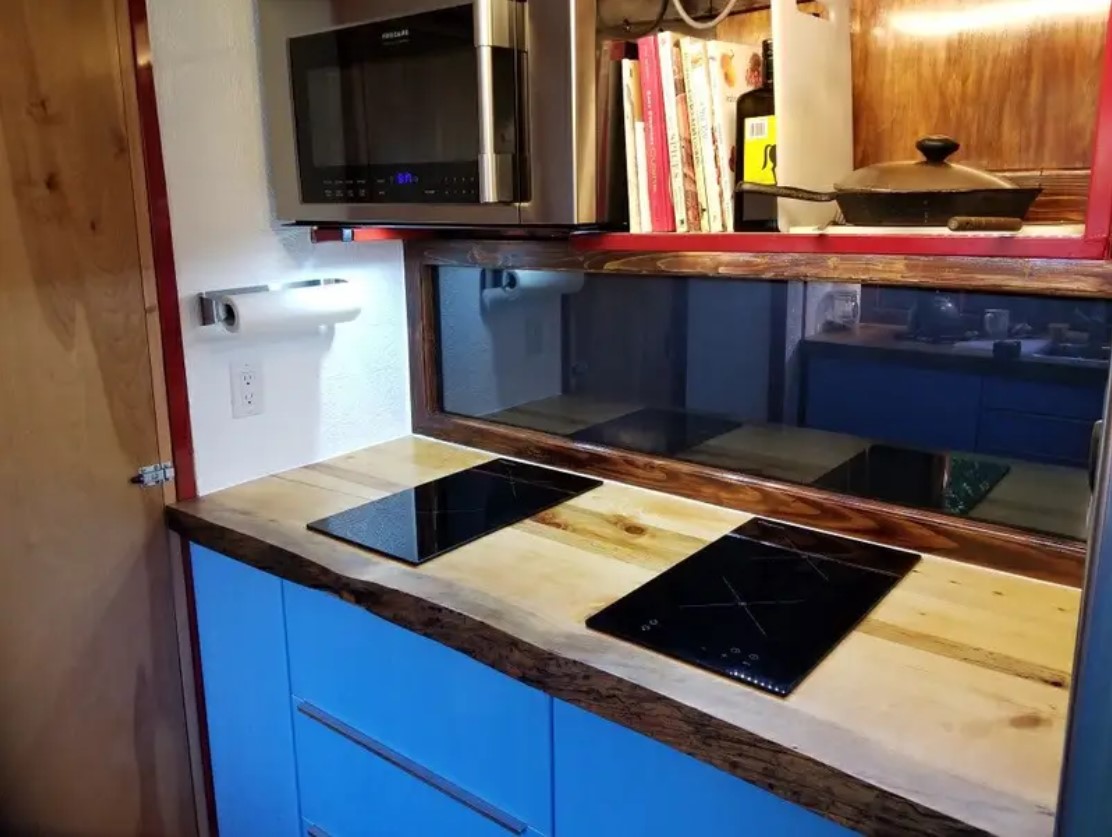 A fitted kitchen with blue cabinets and black cooktops inside the converted trailer.