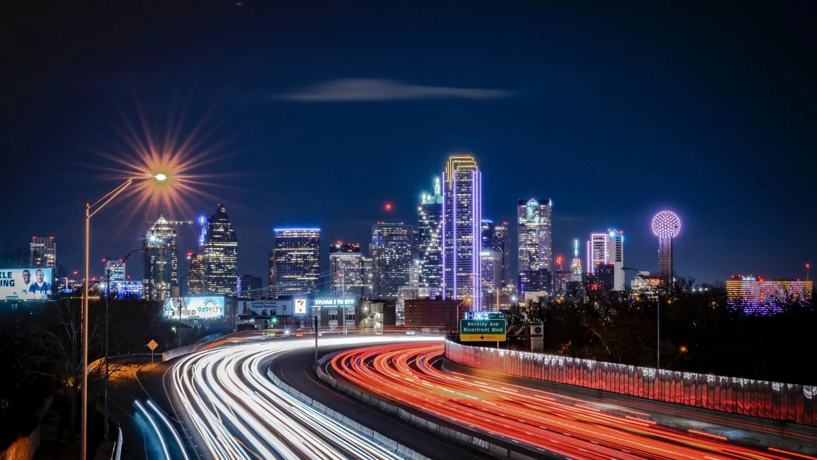 A long-exposure photograph capturing the vibrant nighttime skyline of Dallas, Texas