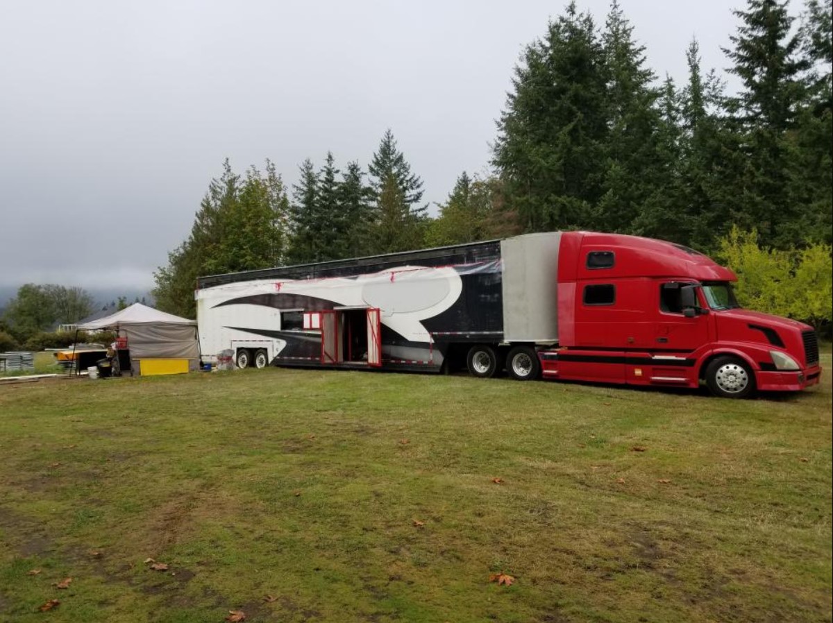 The completed semitrailer home with a red tractor cab parked beside trees.