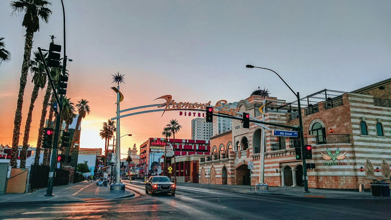 The Fremont East District sign arches over a street in Las Vegas, Nevada, against a backdrop of a sunset sky