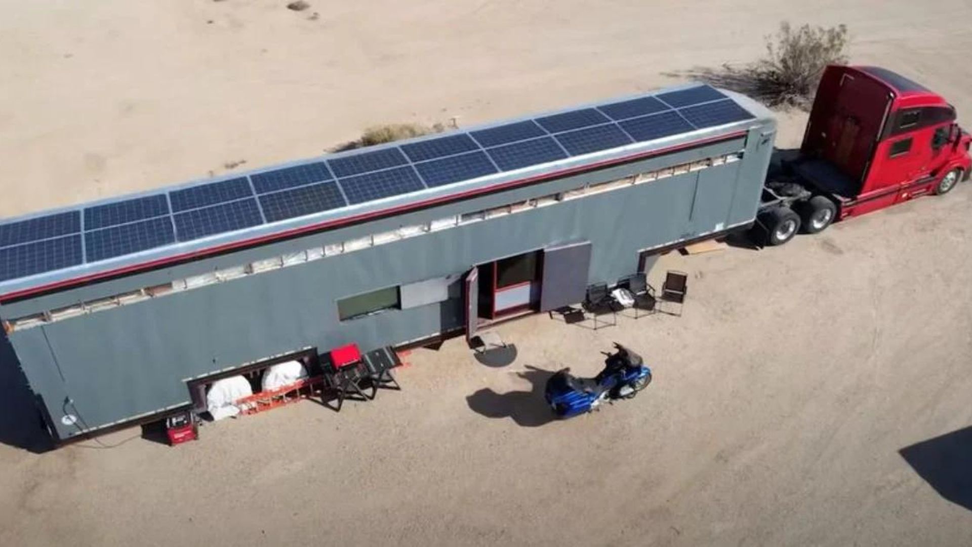 An overhead view of a long semitrailer with rooftop solar panels and a red tractor cab.