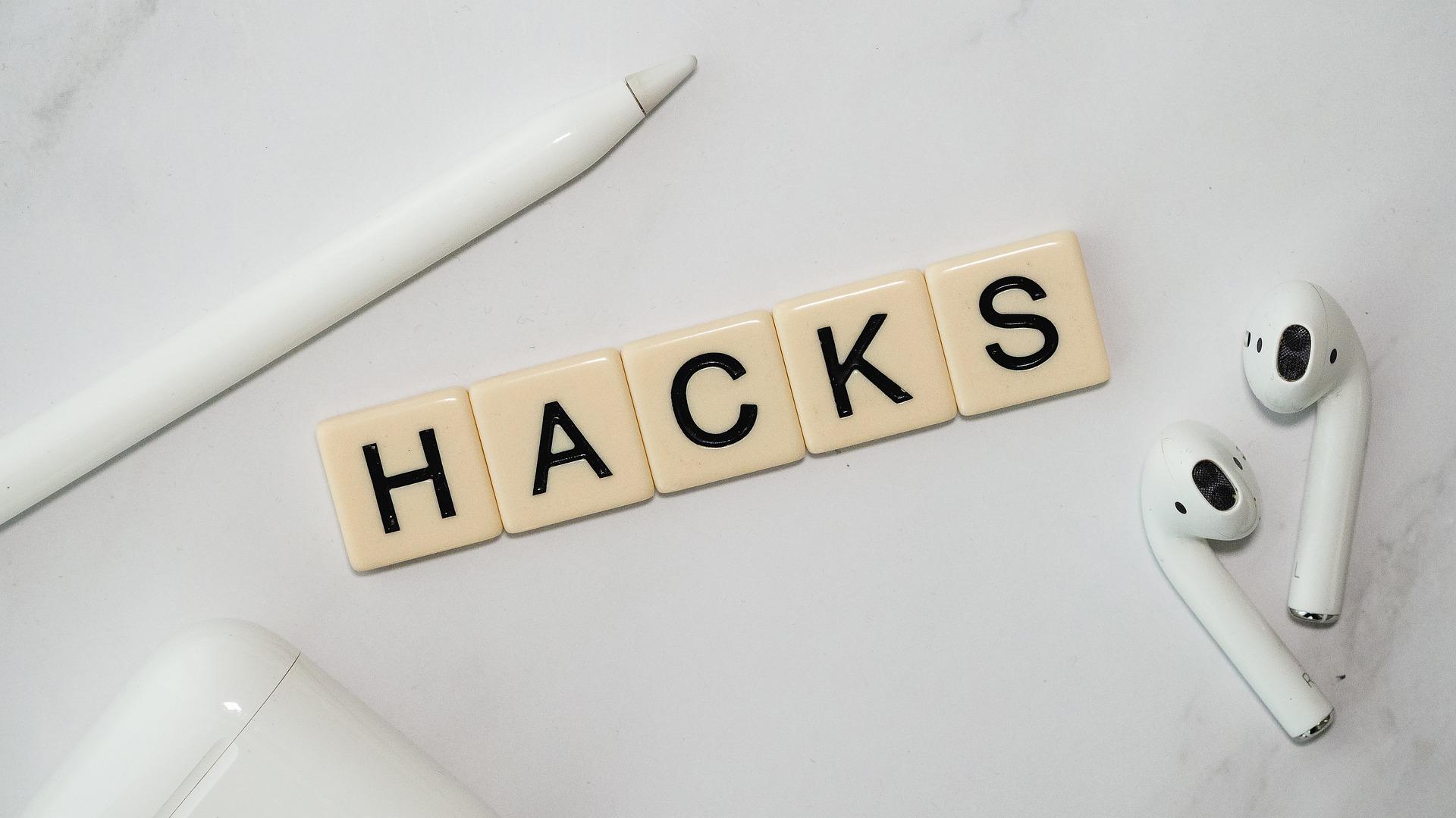 Wooden letter tiles spelling HACKS beside white earbuds and a pen.
