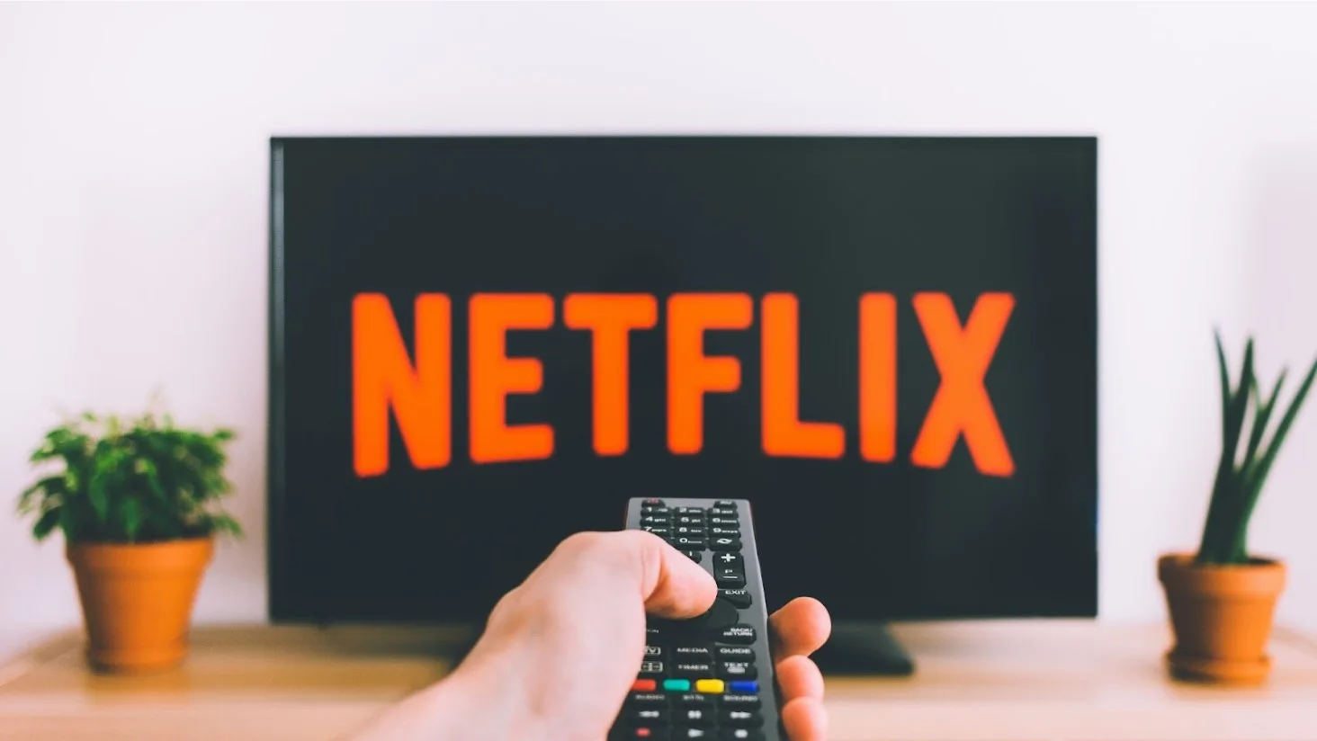 A person holding a remote control aimed towards a television screen displaying the Netflix logo