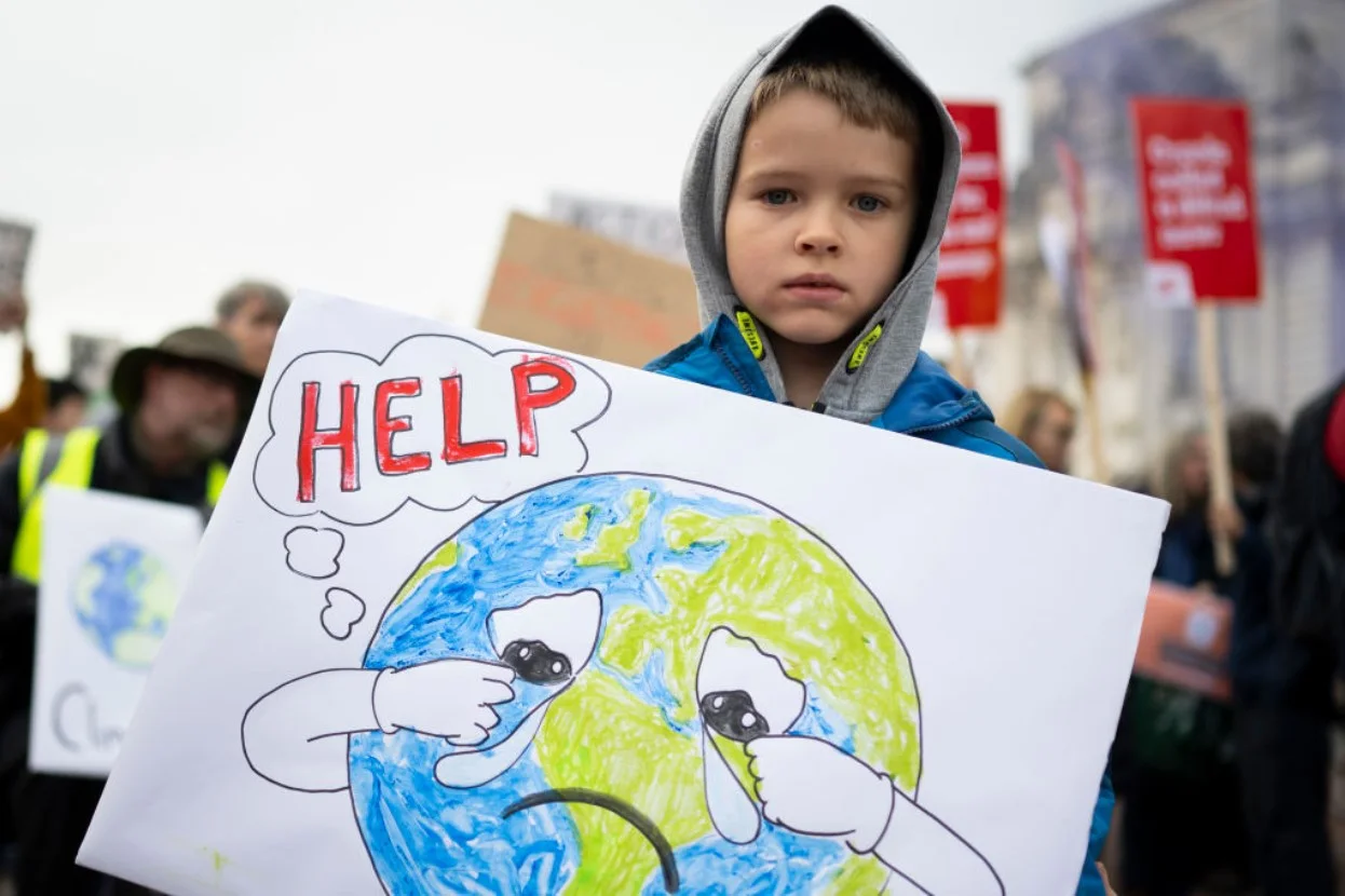 A boy holds a sign saying help during a protest for climate justice with a crying world and the word “Help”