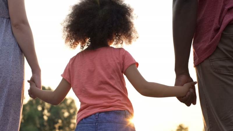 A child holding hands with two adults outdoors