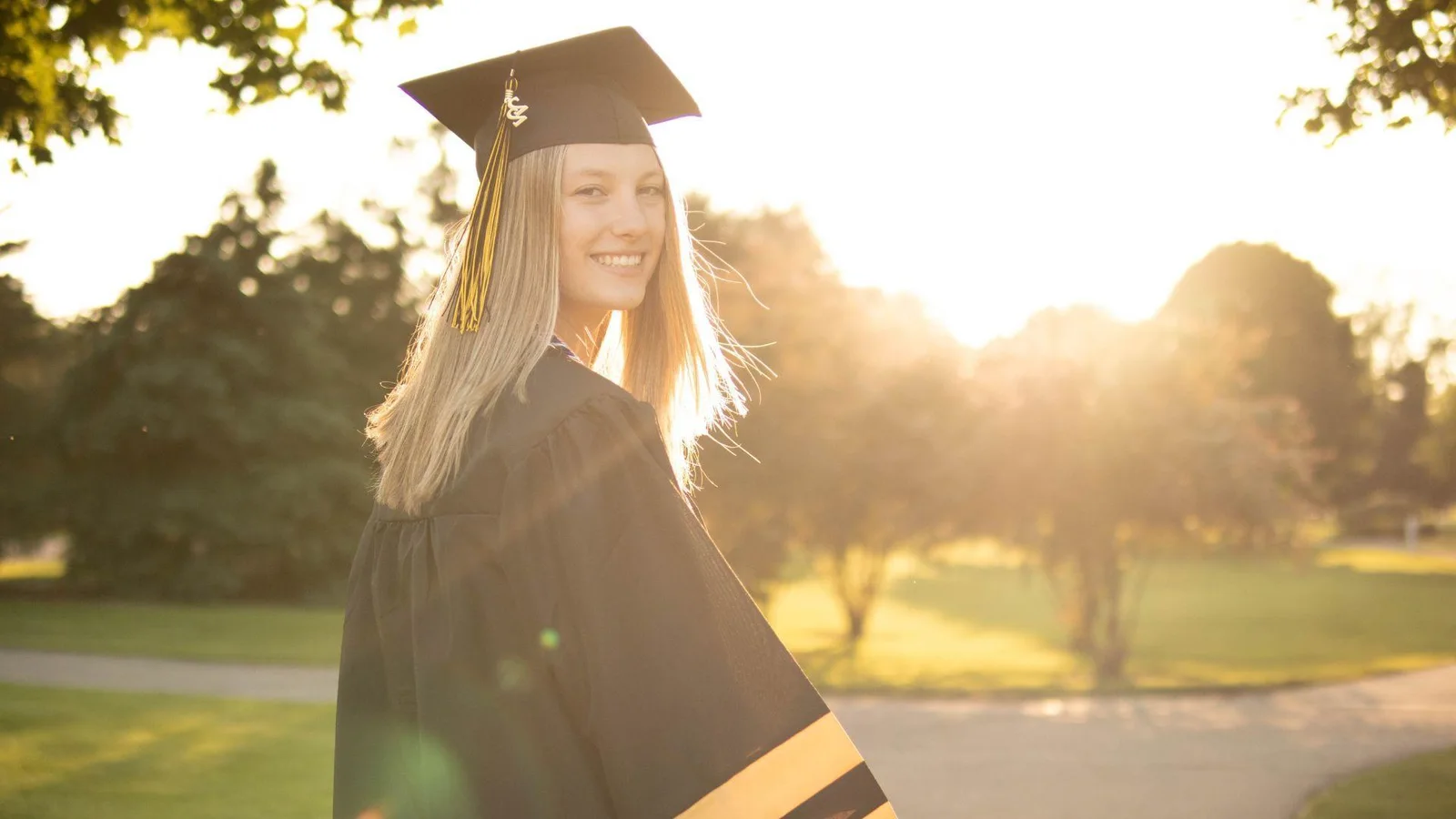 A happy graduate wearing a black and gold cap and gown