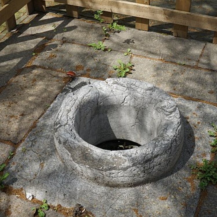 An archive photograph of an old stone well opening outdoors.