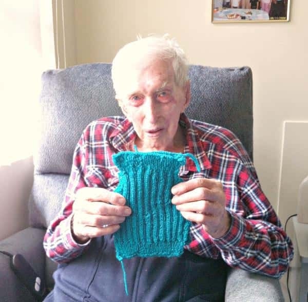 Alfred Date sitting in a chair and holding blue knitting.