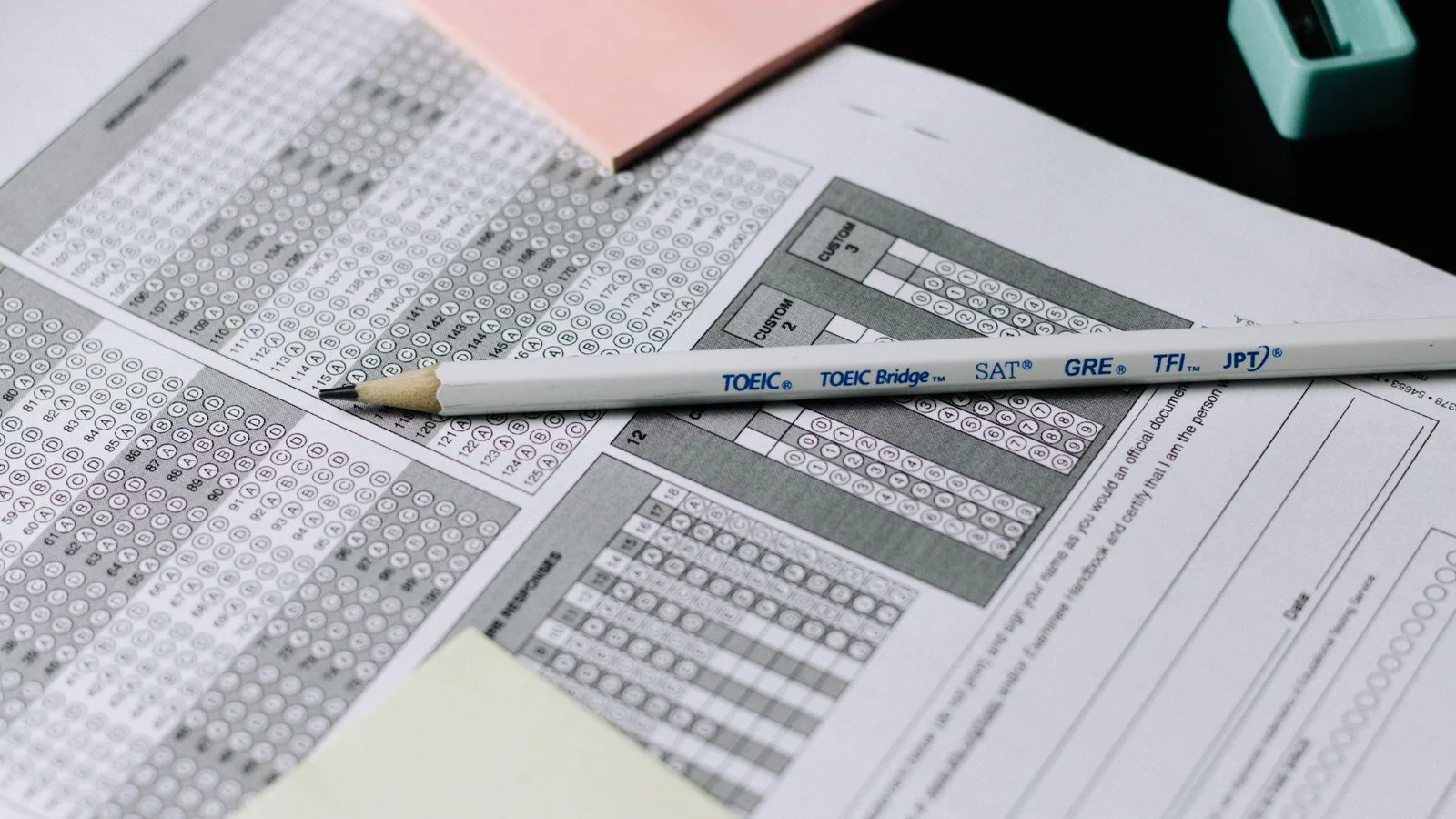 An image displaying multiple standardized test answer sheets alongside a pencil, where circles on the answer sheets can be filled in to answer questions