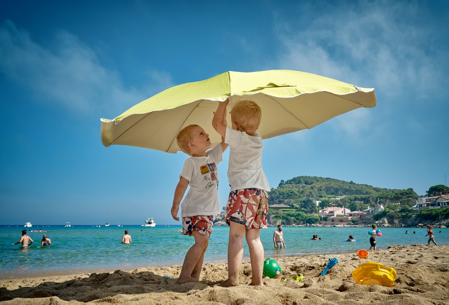 Two children beneath a beach umbrella beside the sea