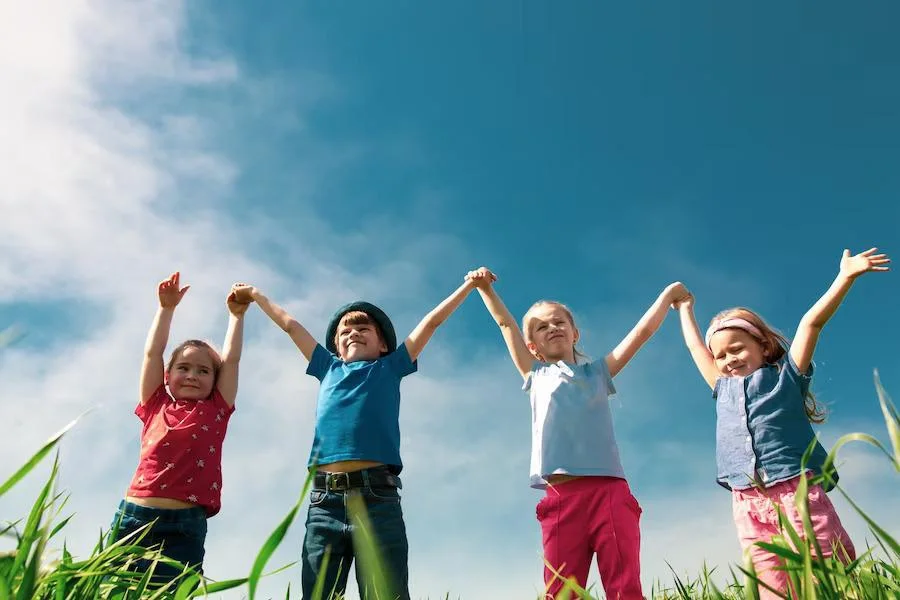 Kids holding hands in the air outside in front of a blue sky