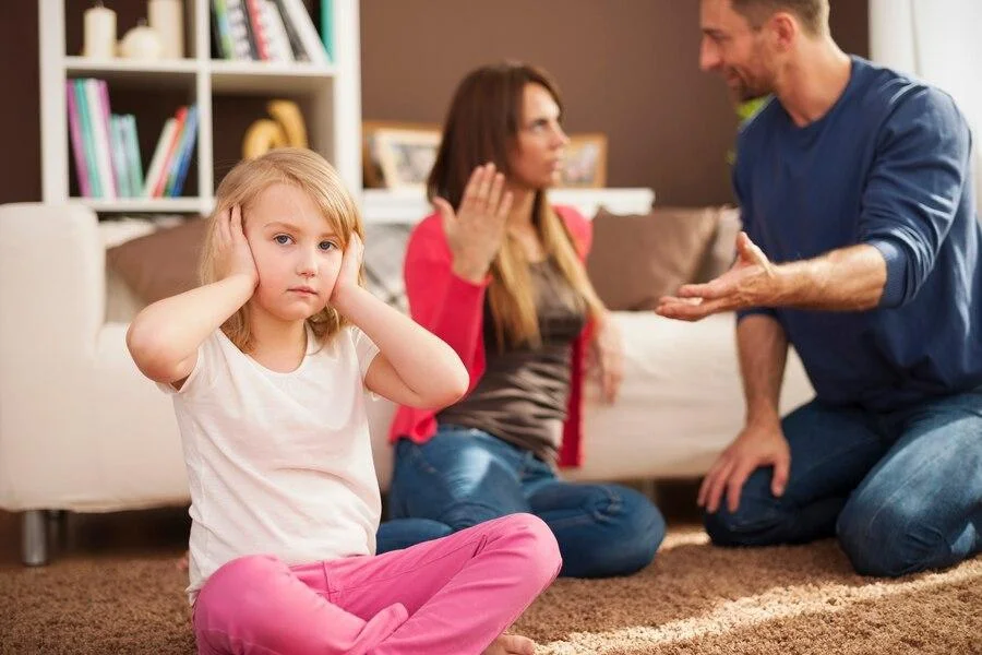 Little girl covering her ears while her parents fight behind her