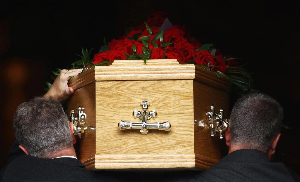Men hold wooden coffin topped with red roses
