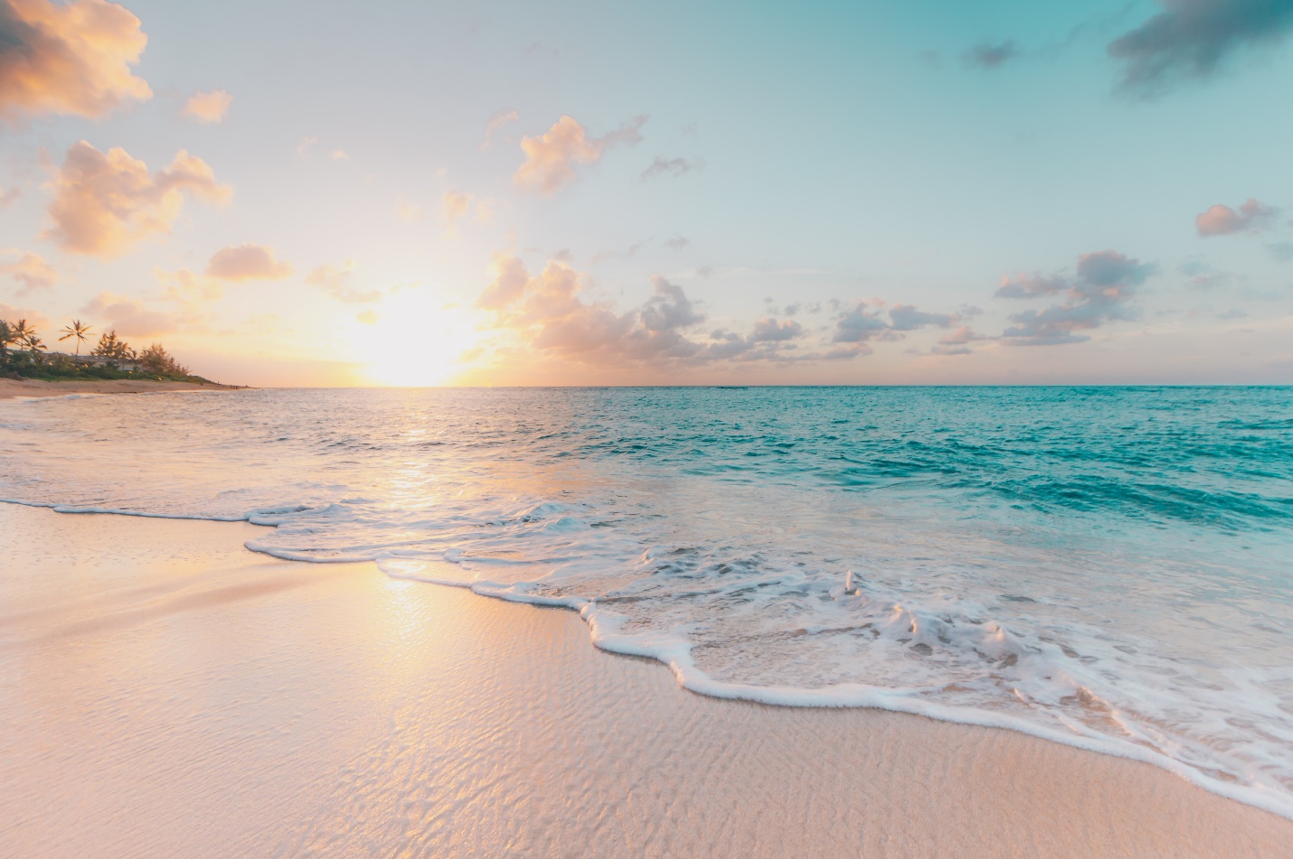 Waves washing onto a sandy beach beneath a pastel sunset.