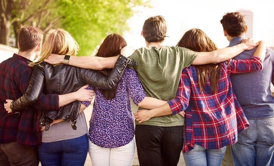 Backs of friends standing in a line with their arms around each other