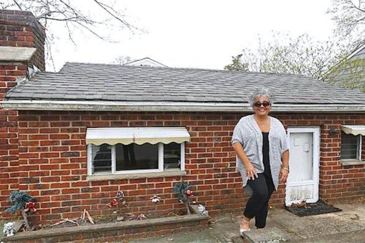 Anna Jones standing beside the small brick cottage on her property.