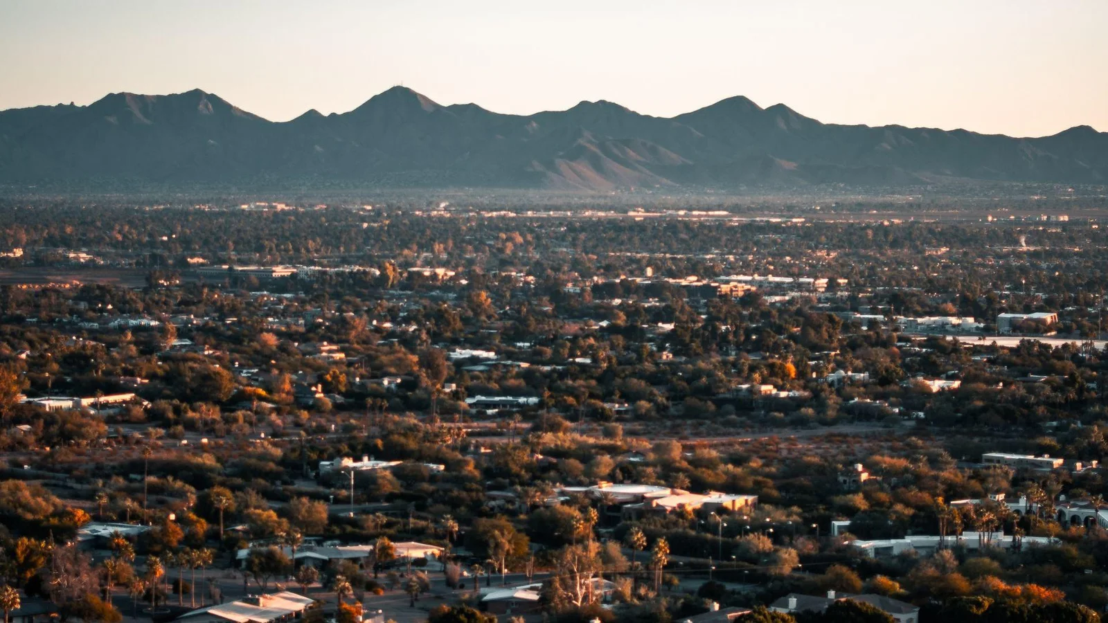 A panoramic view of Tucson, Arizona during golden hour, showcasing the vast, flat expanse of the city with residential and commercial buildings
