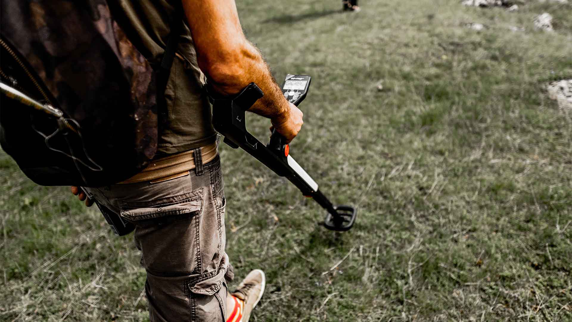 Illustrative photograph of a person using a metal detector on grass.