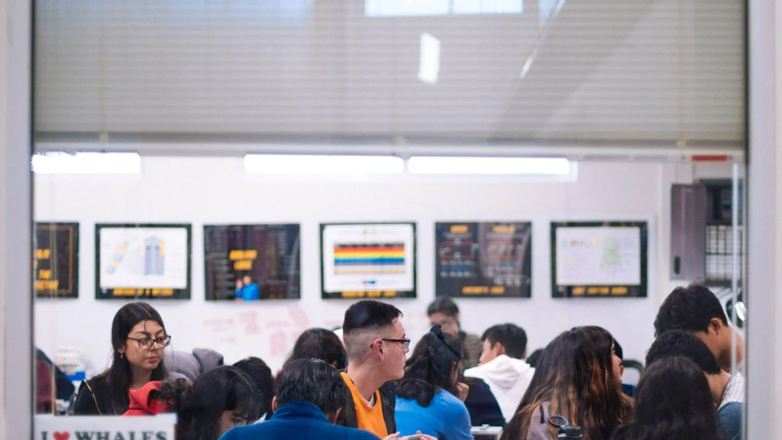 View through a window into a classroom filled with students. The students appear engaged and focused